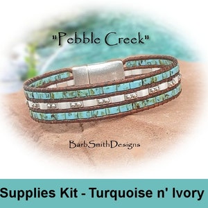 May include: A turquoise and ivory beaded bracelet with silver accents and a magnetic clasp. The bracelet is labeled "Pebble Creek" and "BarbSmithDesigns". Supplies Kit - Turquoise n' Ivory.