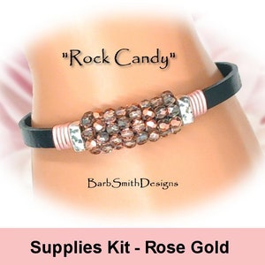 Può includere: Un braccialetto in pelle nera con un ciondolo in oro rosa e argento. Il ciondolo è fatto di piccoli cristalli sfaccettati in tonalità di marrone e oro rosa. Il braccialetto è etichettato "Rock Candy" e "Supplies Kit - Rose Gold".