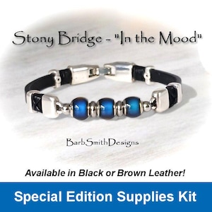 May include: A black leather bracelet with silver accents and blue iridescent beads. The bracelet is available in black or brown leather. The text "Stony Bridge - "In the Mood"" is visible above the bracelet. The text "Barb Smith Designs" is visible below the bracelet. The text "Available in Black or Brown Leather!" is visible below the bracelet. The text "Special Edition Supplies Kit" is visible at the bottom of the image.