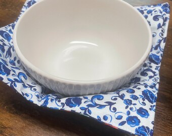 Peut inclure: Un bol en céramique blanche avec un motif floral bleu et blanc à l'extérieur. Le bol est posé sur un dessous de plat en tissu floral bleu et blanc.