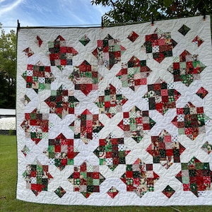 May include: A white quilt with a Christmas theme. The quilt is made up of squares of red, green, and white fabric with various Christmas patterns. The quilt is hanging on a clothesline.