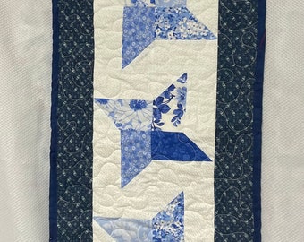 Peut inclure: Un chemin de table blanc avec un motif floral bleu et blanc. Le chemin de table a une bordure bleu foncé avec un motif décoratif. Cinq étoiles bleues et blanches sont centrées sur le chemin de table.