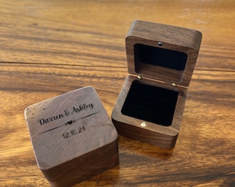 Op de afbeelding: Een houten ringendoos met een donkerbruine afwerking. De doos is gegraveerd met de tekst "Darren & Ashley" en de datum "12.10.24".