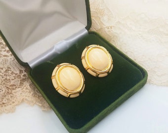 May include: A pair of oval-shaped earrings with a white center and gold trim. The earrings are in a green velvet box.