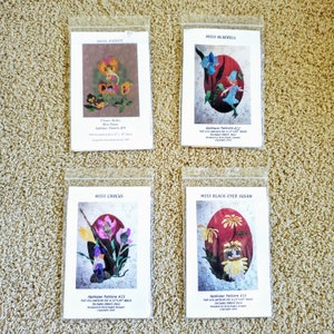 May include: Four different applique patterns for quilting, each featuring a different flower: Miss Pansy, Miss Bluebell, Miss Crocus, and Miss Black-Eyed Susan. Each pattern is printed on white paper and includes instructions for a 22" x 30" block.