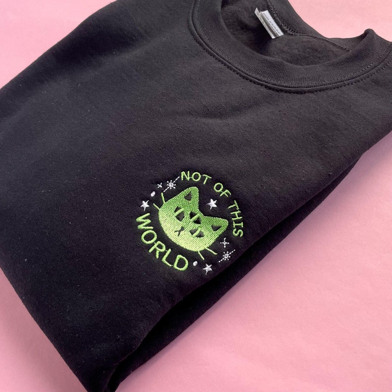 May include: Black sweatshirt with a green embroidered design of a cat with the text "Not of this world" around it.