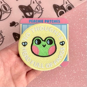 May include: A yellow embroidered patch with a green frog with pink cheeks and the text "No thoughts head full of frogs" in white.