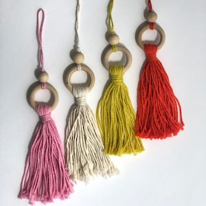 May include: Four wooden ring tassels with different colored yarn. The tassels are pink, white, yellow, and orange.