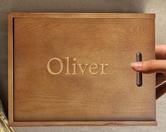 May include: A wooden box with a hinged lid and a handle on the side. The box is engraved with the name "Oliver".