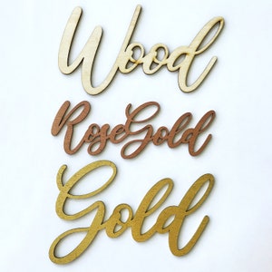 May include: Three wooden words in different colors: "Wood" in natural wood, "Rose Gold" in rose gold, and "Gold" in gold.
