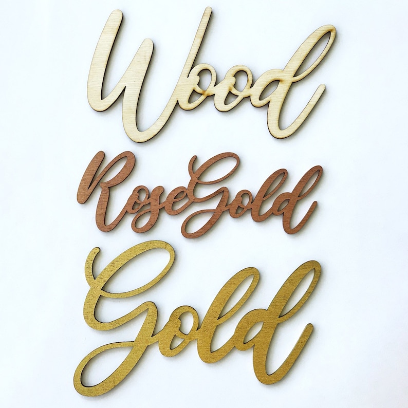 May include: Three wooden words in different colors: "Wood" in natural wood, "Rose Gold" in rose gold, and "Gold" in gold.