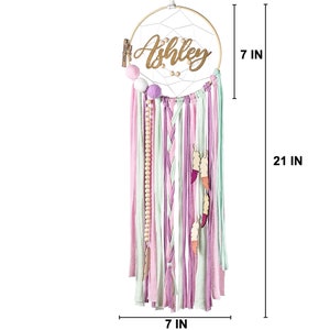 May include: A pink, green, and white dream catcher with the name "Ashley" written on it. The dream catcher is 7 inches in diameter and 21 inches long.