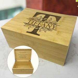 May include: A bamboo box with a hinged lid. The lid is engraved with the name "TIFFANY" in a decorative font, with a floral design. The box is open, revealing an empty interior. The inside of the lid has engraved text.