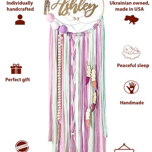 May include: A pink, green, and white dreamcatcher with wooden beads and feathers. The dreamcatcher has a wooden hoop with the name "Ashley" written in gold glitter. The dreamcatcher is handmade and comes with hanging hardware.