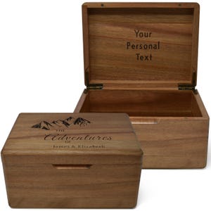 May include: Wooden keepsake box with a hinged lid, open to reveal the interior. The closed box has the text "The Adventures of James & Elizabeth" and a mountain graphic. The open box has the text "Your Personal Text".