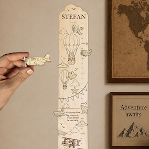 May include: A light-colored wooden growth chart featuring engraved illustrations of airplanes, hot air balloons, clouds, and stars. The chart includes the name STEFAN, measurement markings, and the text No matter how big you grow... You'll always be our baby.