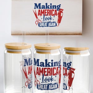 May include: Three clear glass tumblers with bamboo lids and straws. The tumblers feature the text "Making America Look Great Again" in red and blue, along with barber scissors and a clipper design. A wooden sign with the same design hangs above.