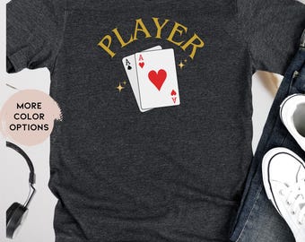 May include: Dark grey heather t-shirt with the word "PLAYER" in gold lettering and two playing cards with aces showing. The cards are a spade and a heart.