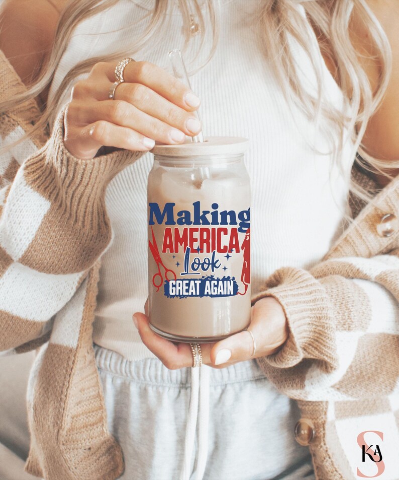 May include: A clear glass tumbler with a wooden lid and a glass straw, filled with a light brown beverage. The tumbler features the text "Making America Look Great Again" in red, white, and blue, with scissors and a comb graphic.