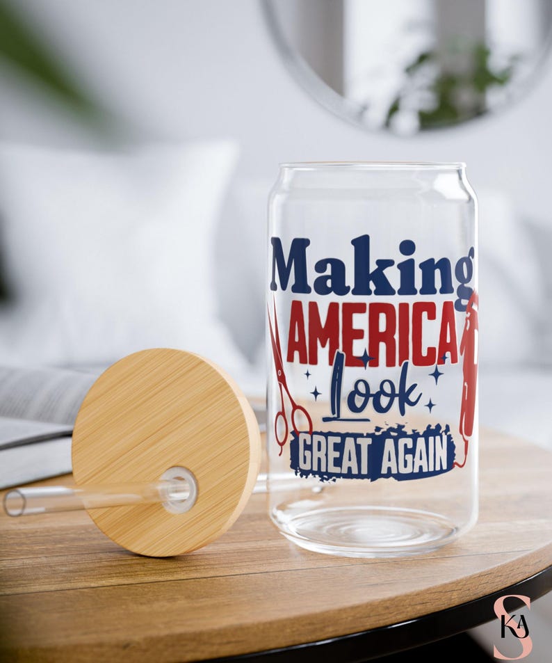May include: A clear glass can-shaped tumbler with a wooden lid and straw. The tumbler features the text "Making America Look Great Again" in red and blue, along with barber tools. The lid is made of light brown wood.
