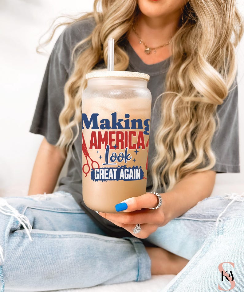 May include: A clear glass tumbler with a bamboo lid and straw, filled with a light brown beverage. The tumbler features the text "Making AMERICA Look GREAT AGAIN" in red, white, and blue, with scissors and star graphics.