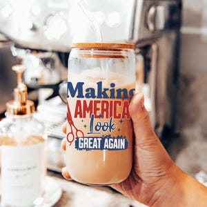 May include: A clear glass tumbler with a wooden lid and a straw, filled with a creamy beverage. The tumbler features the text "Making America Look Great Again" in blue and red, with scissors and star graphics.