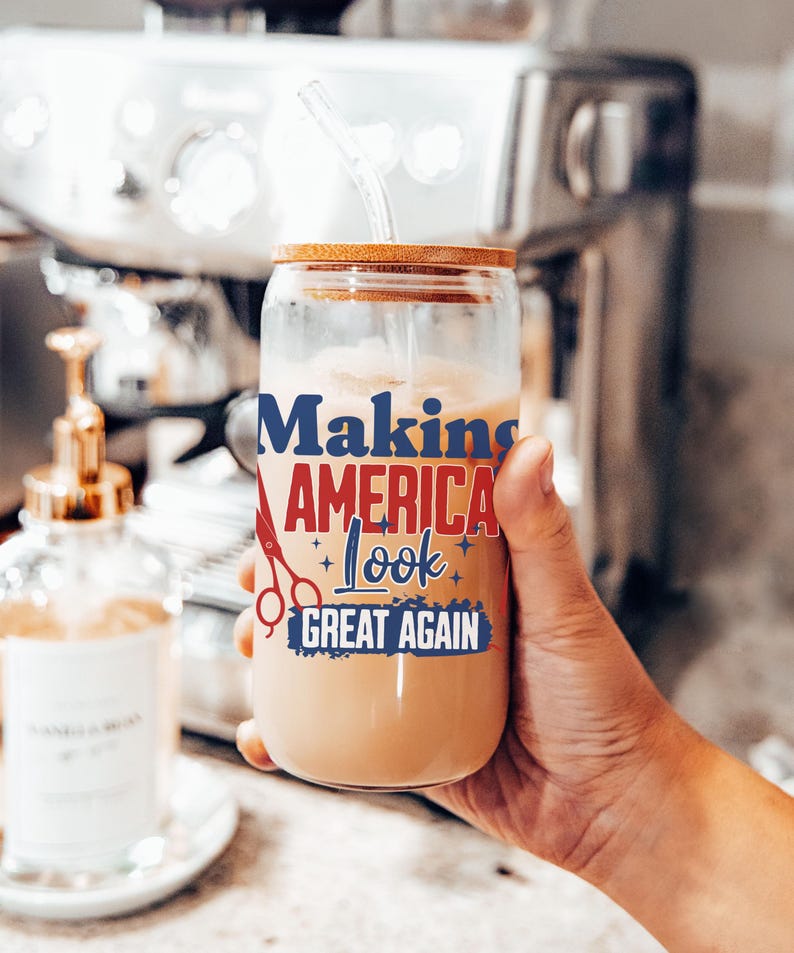 May include: A clear glass tumbler with a wooden lid and a straw, filled with a creamy beverage. The tumbler features the text "Making America Look Great Again" in blue and red, with scissors and star graphics.