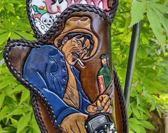 May include: Hand-tooled leather holster depicting a cowboy with a cigarette, holding a gun, and a bottle of liquor. The holster has playing cards and the word "GAM" on the top. The colours include brown, blue, and tan.