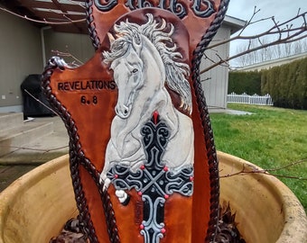 May include: A brown leather holster with a white horse and a black and silver cross design. The holster has the word "JAKE" and "REVELATIONS 6:8" embossed on it.