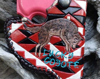 May include: A red, black and white leather holster with a coyote design and the words "Lucky Coyote" embroidered in blue. The holster is designed to hold a small pink handgun.
