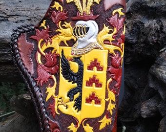 May include: A brown leather holster with a detailed design of a coat of arms featuring a black eagle, red and yellow accents, and the name "Teekema" embossed on the bottom.