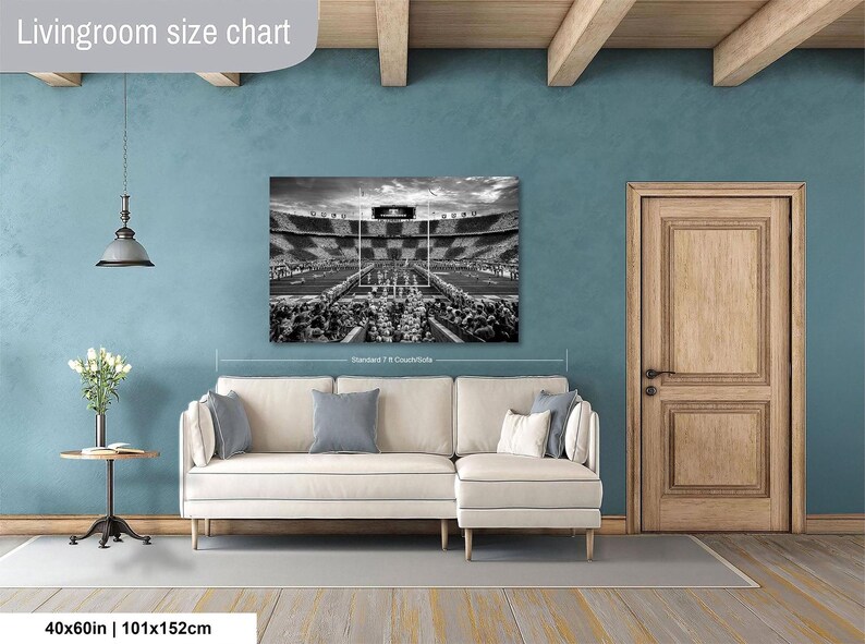 a living room with a large black and white photograph of a stadium on the wall, a white sofa, a wooden door, and a small table with a vase of flowers.