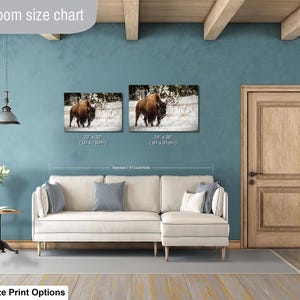 a living room with a white sofa, a wooden door, and a painting of a bison on the wall. The living room has a blue wall and a wooden ceiling.