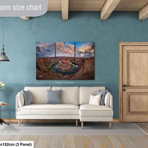 The image is a living room with a large, three-panel landscape painting hanging on the wall. The painting depicts a scenic view of a canyon with a river winding through it. The room has a white sofa and a wooden door, creating a cozy and inviting atmosphere.