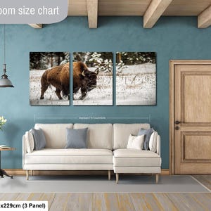 The image is a living room with a large wall art piece depicting a bison in a snowy field. The living room has a white sofa and a wooden door, and the wall art is approximately 40 inches wide and 101.29 cm in height.