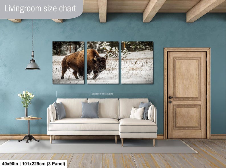 The image is a living room with a large wall art piece depicting a bison in a snowy field. The living room has a white sofa and a wooden door, and the wall art is approximately 40 inches wide and 101.29 cm in height.