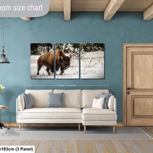 The image is a living room with a large wall art depicting a bison in a snowy field. The living room has a white sofa and a wooden door.