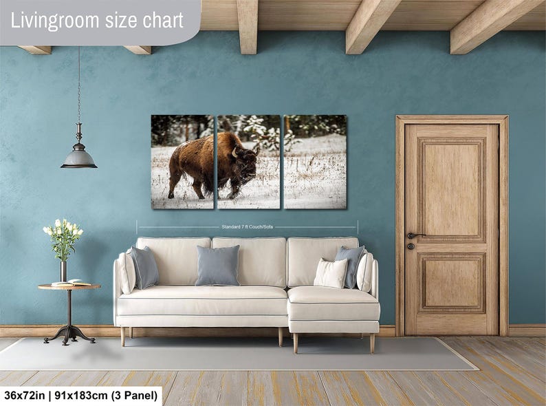 The image is a living room with a large wall art depicting a bison in a snowy field. The living room has a white sofa and a wooden door.