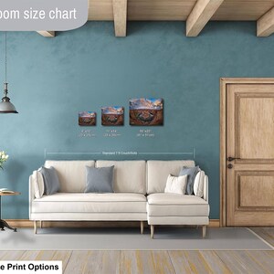 a living room with a white sofa, a wooden door, and a hanging light fixture. There are three framed artworks displayed on the wall, each with different sizes and dimensions. The living room appears to be well-decorated and spacious.