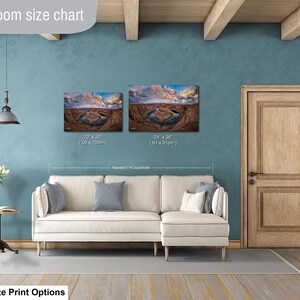 a living room with a white sofa, a wooden door, and a painting of a desert landscape on the wall. The living room appears to be well-lit and decorated with a potted plant and a vase.