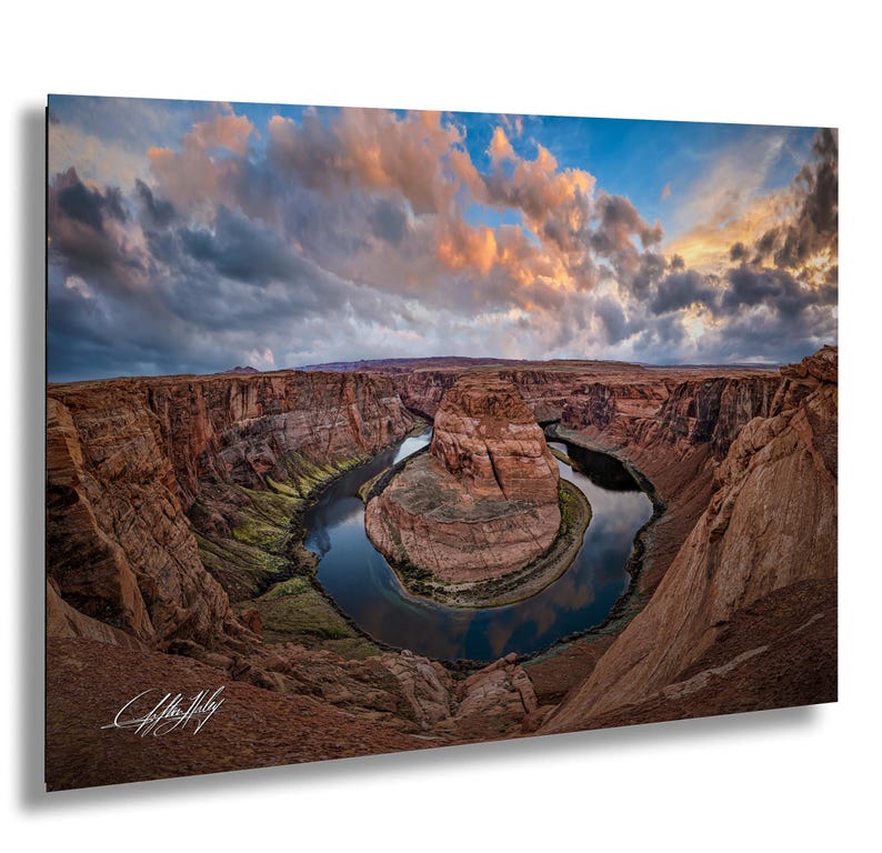 a stunning natural landscape with a winding river surrounded by towering red rock formations. The sky above is filled with clouds, creating a dramatic backdrop for the scene. The photograph is taken from a high vantage point, offering a panoramic view of the canyon and the river.
