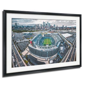 An aerial view of a large sports stadium surrounded by a city skyline, with the stadium's field and surrounding parking lots visible.