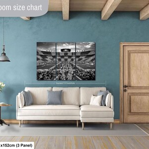 a living room with a large black and white photograph of a stadium or arena displayed on the wall. The room has a white sofa, a wooden door, and a wooden floor.