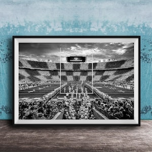 A black and white photograph of a crowded football stadium with a large audience, featuring a scoreboard and field markings.