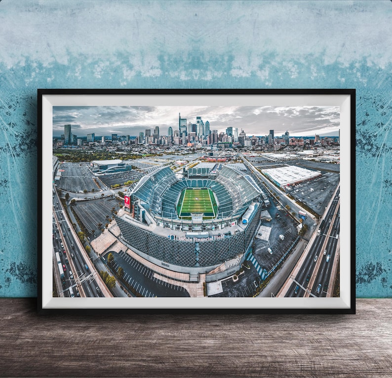 An aerial view of a large sports stadium surrounded by a city skyline, with the stadium's field and surrounding parking lots visible.
