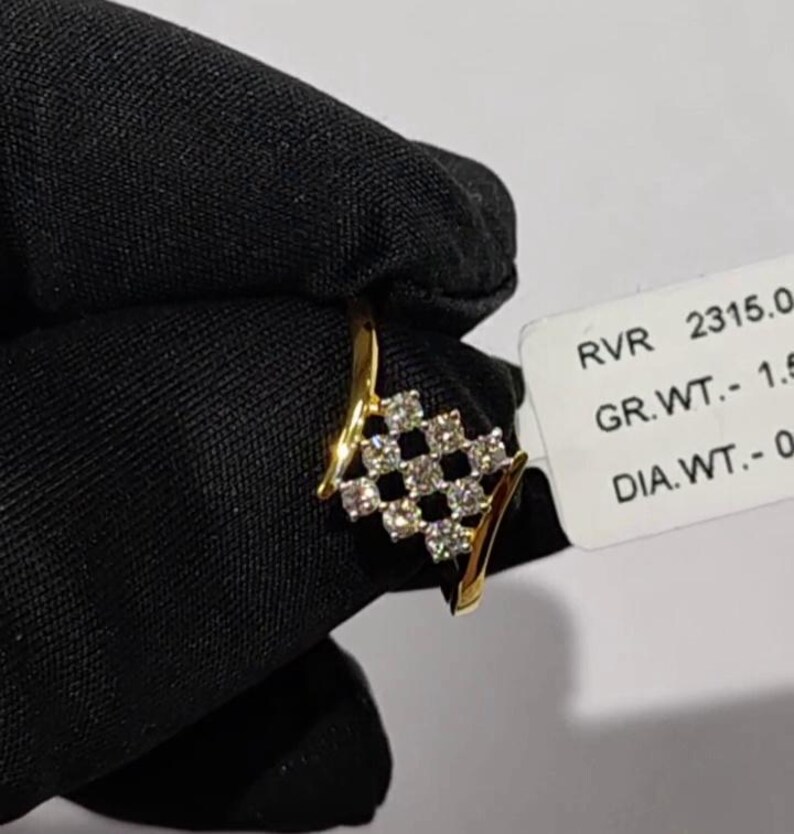 May include: A gold ring with a diamond-studded, checkered design. The ring features a series of small, clear diamonds set in a square pattern. The ring is held against a black background, with a price tag visible.