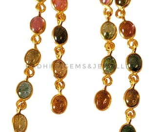 May include: Gold earrings with a multi-colored gemstone drop. The earrings feature a chain of oval-shaped gemstones in shades of green, pink, and brown.