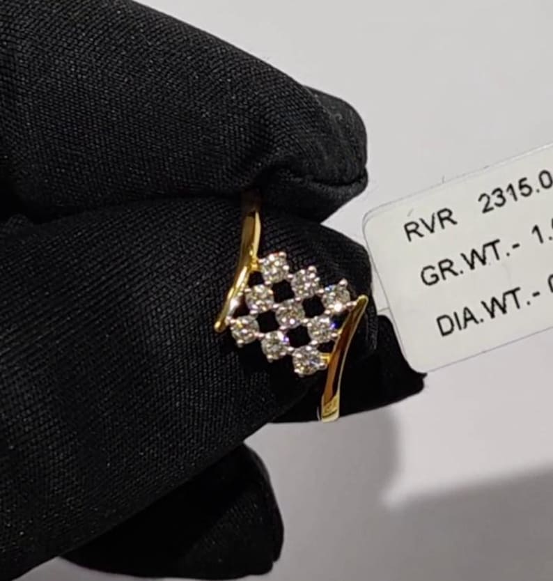 May include: A gold ring with a diamond-studded checkerboard design. The ring has a curved band and a cluster of diamonds set in a square pattern. The ring is held against a black background.