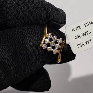 May include: A gold ring featuring a cluster of diamonds in a checkered pattern. The ring has a curved design with a band that splits into two graceful arcs. The diamonds are set in a square arrangement, creating a sparkling effect.