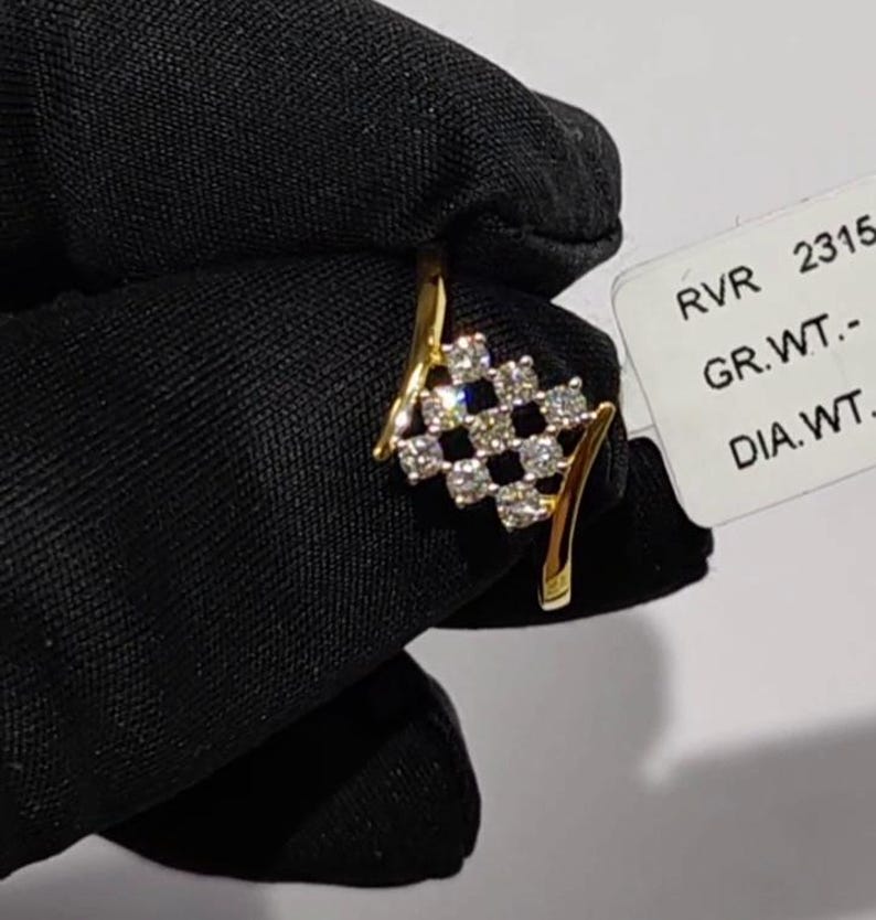 May include: A gold ring featuring a cluster of diamonds in a checkered pattern. The ring has a curved design with a band that splits into two graceful arcs. The diamonds are set in a square arrangement, creating a sparkling effect.